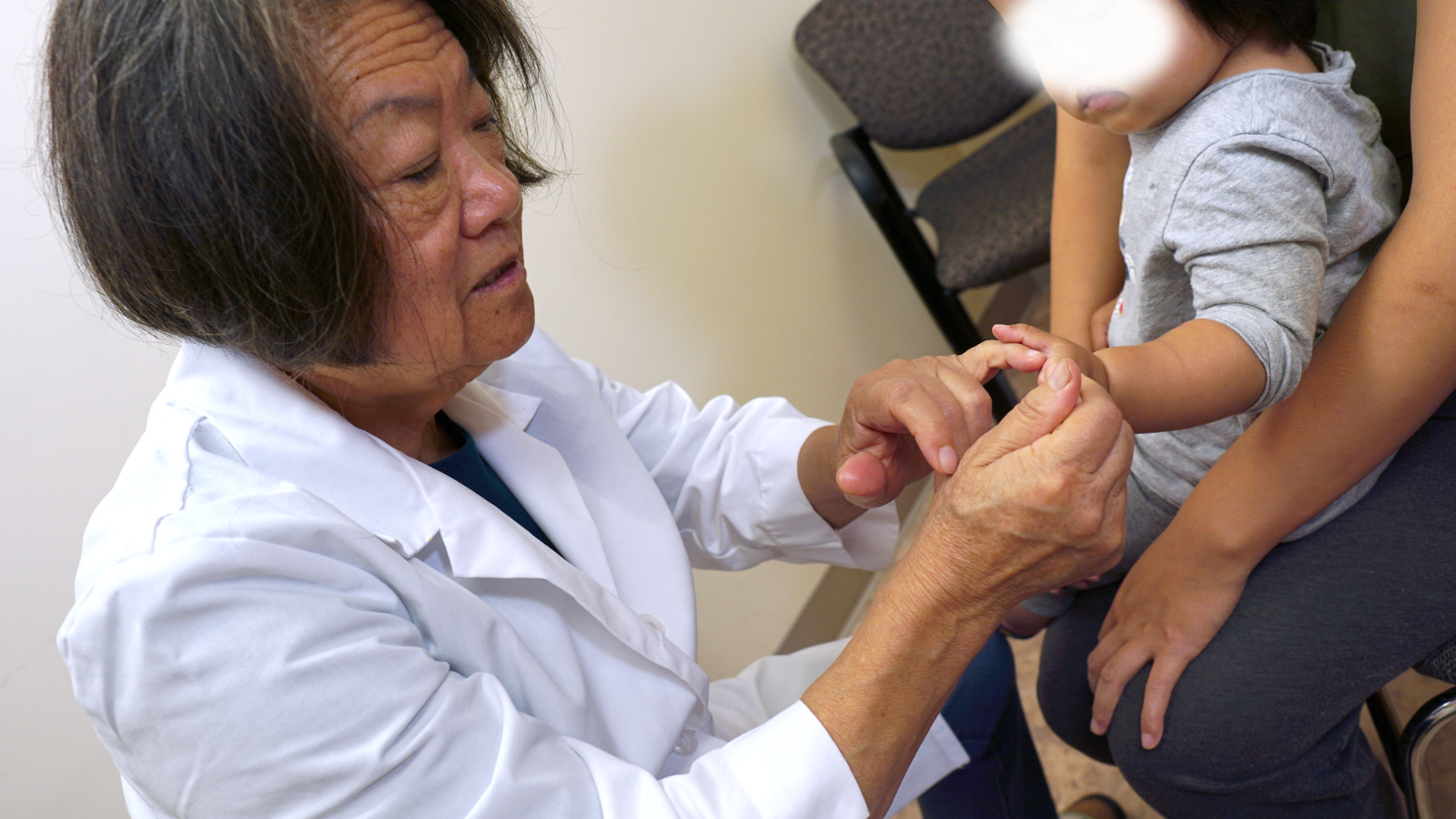 Traditional Chinese Medicine practitioner in a white coat gently examining a child's hand during a pediatric consultation at a California TCM school